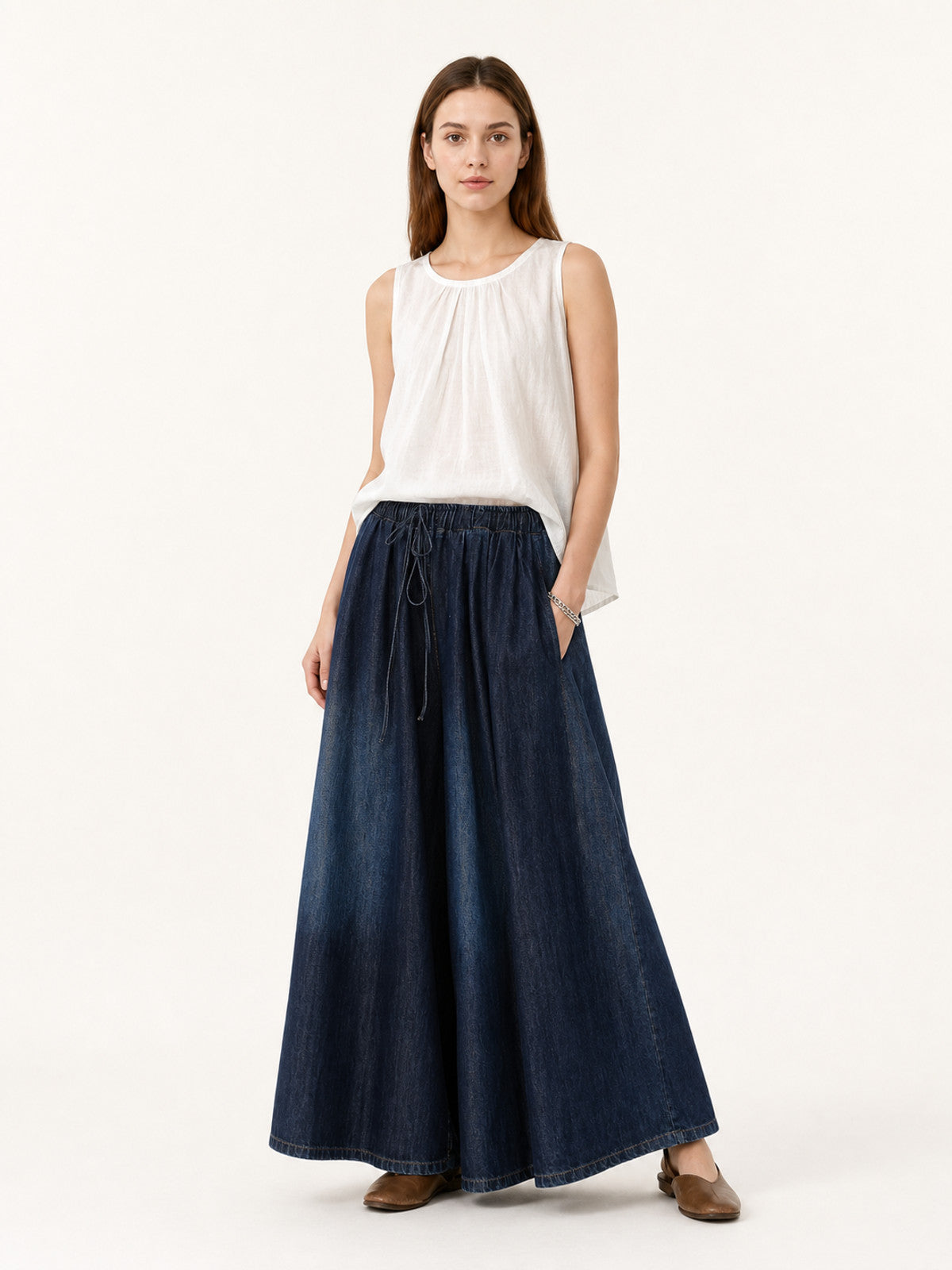 Full-body model wearing dark blue denim-look palazzo pants with a drawstring waist, styled with a sleeveless white top