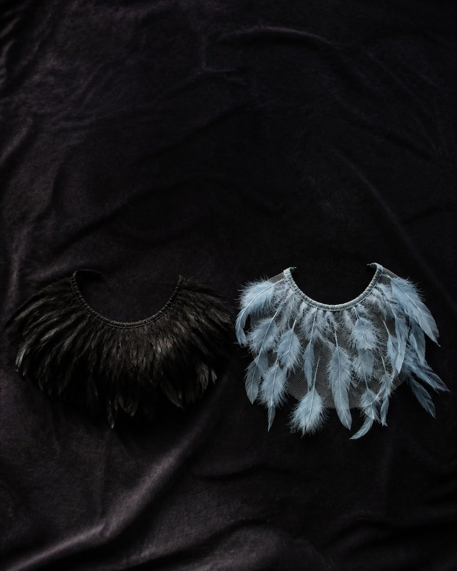 Overhead flat-lay comparing a dense opaque black feather collar with a see-through pale blue sheer mesh feather collar on dark velvet