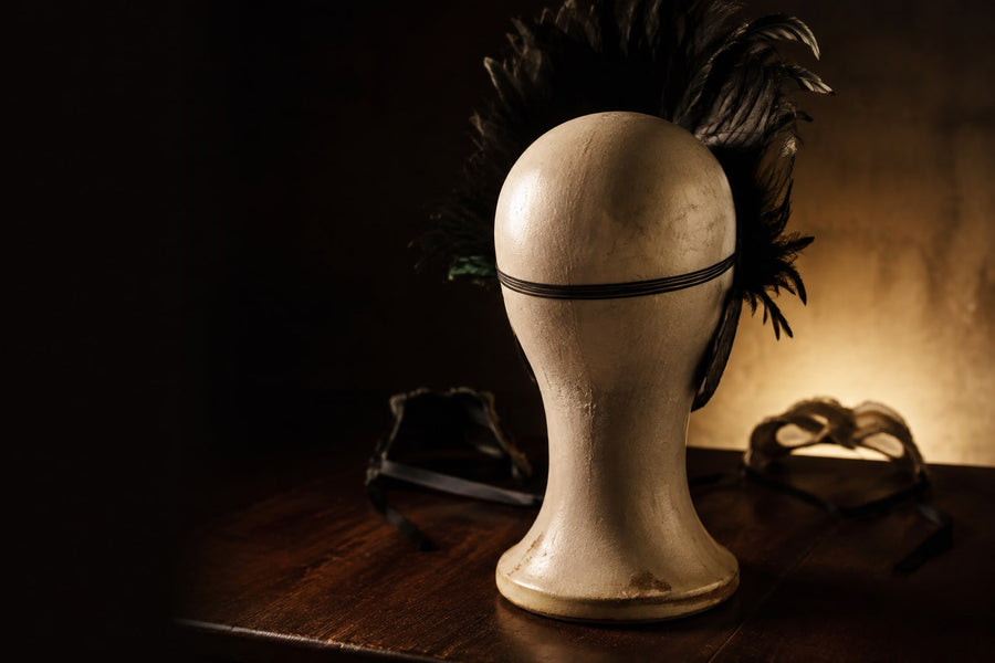 Back of a plaster milliner's head showing the black elastic band that holds a feathered masquerade mask on