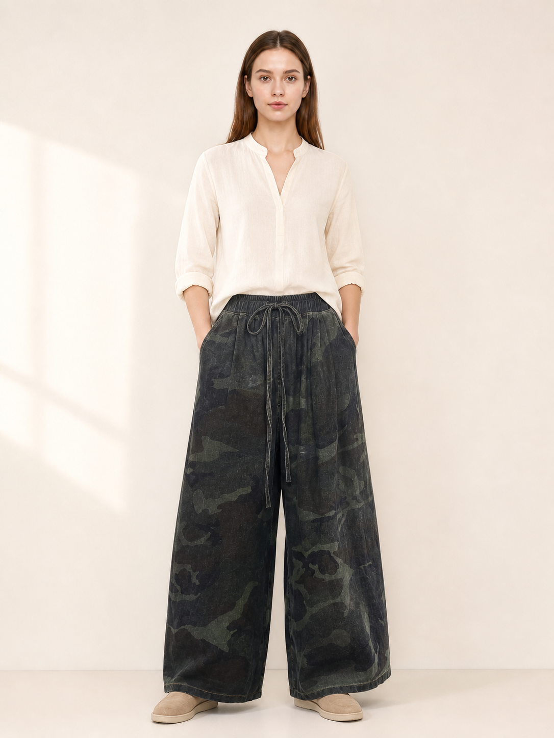 Dark camouflage wide-leg jeans shown full-body on a model, featuring a drawstring waist, side pockets, and cropped hems
