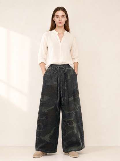 Dark camouflage wide-leg jeans shown full-body on a model, featuring a drawstring waist, side pockets, and cropped hems