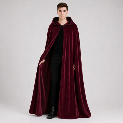 Full-body male model wearing a burgundy velvet-textured hooded cape over black clothing, with the front clasp fastened