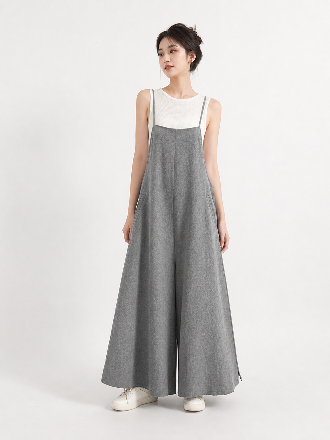 Full-body model wearing gray wide-leg overalls over a white sleeveless top, with thin straps and white sneakers