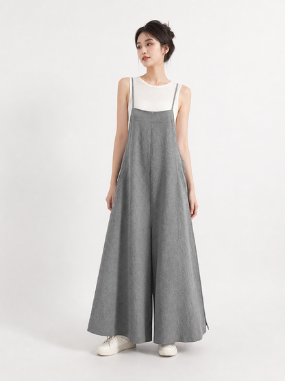 Full-body model wearing gray wide-leg overalls over a white sleeveless top, with thin straps and white sneakers