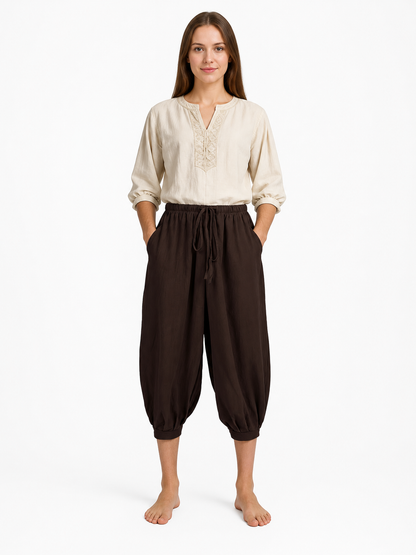 Brown cropped harem pants shown full-body on a model against a white background, with a drawstring waist, pockets and elastic cuffs