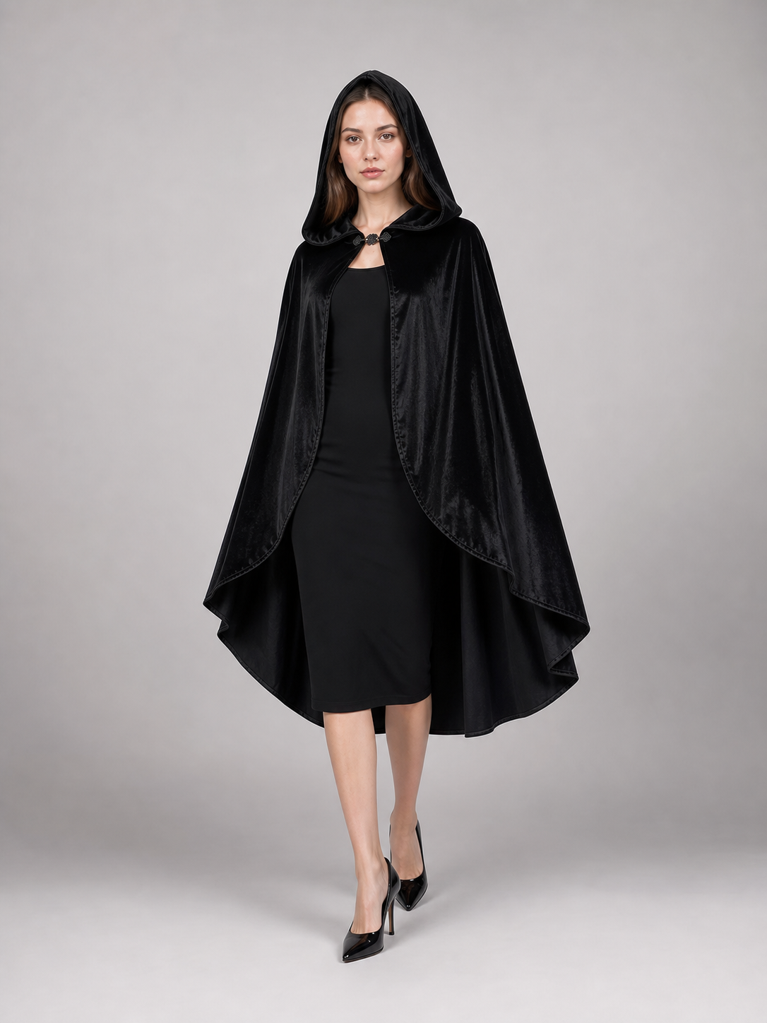 Black hooded cape with a clasp and layered flowing edges, shown full length on a model against a gray studio background