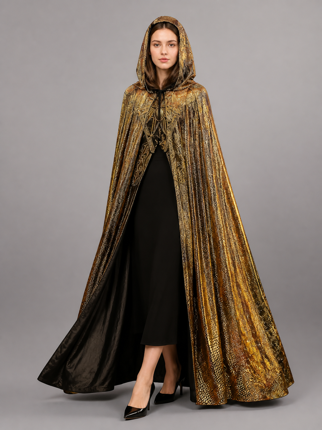 Front view of a model in a gold hooded cape with black lining, draped over a black dress