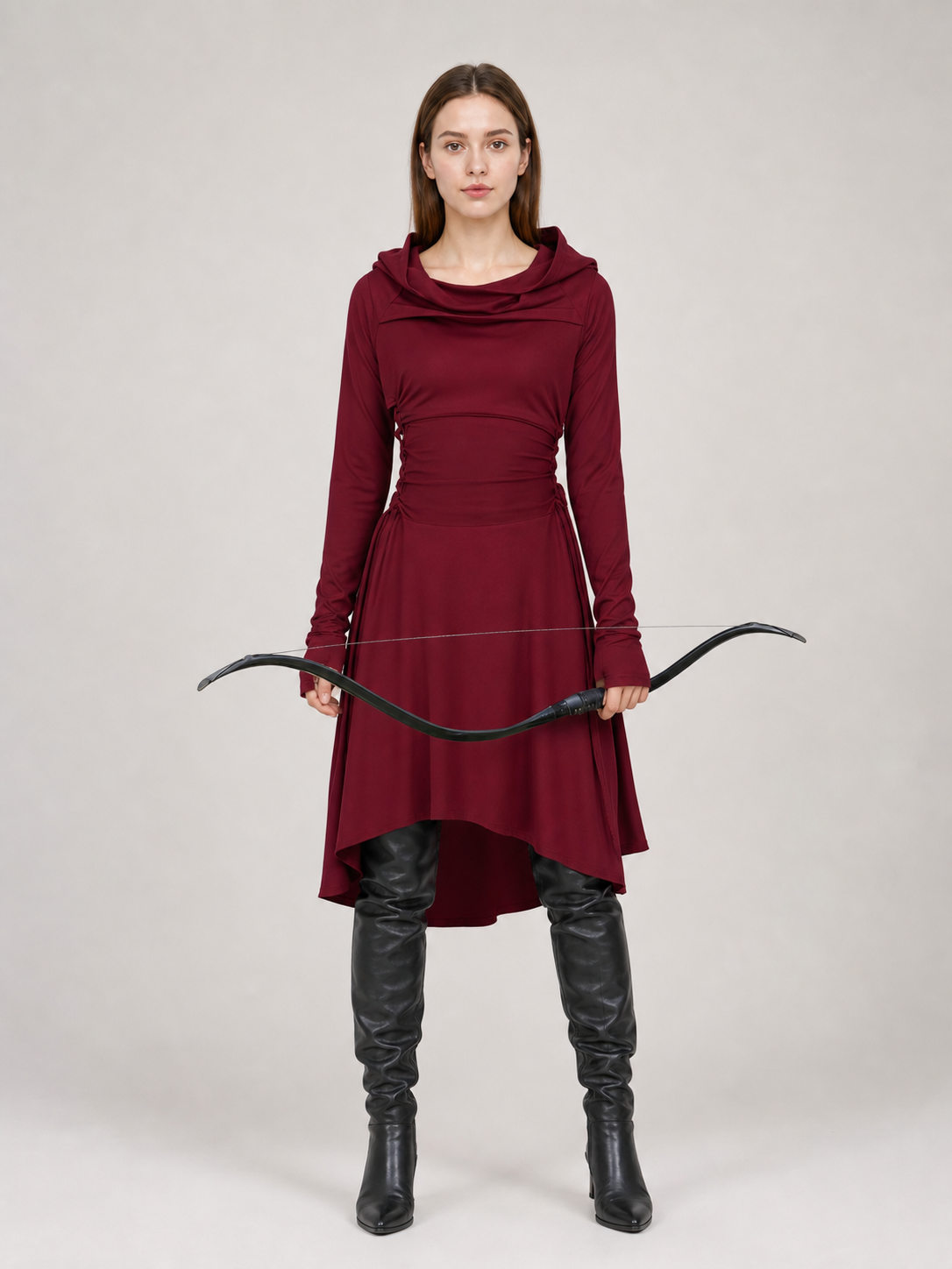 Burgundy hooded tunic in smooth fabric, shown full-body on a model with long sleeves, draped neckline, uneven hem, black boots, and a bow 2