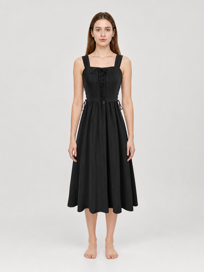 Black midi dress shown full-body on a model, with wide shoulder straps, lace-up bodice, side waist ties, and a gathered flowing skirt
