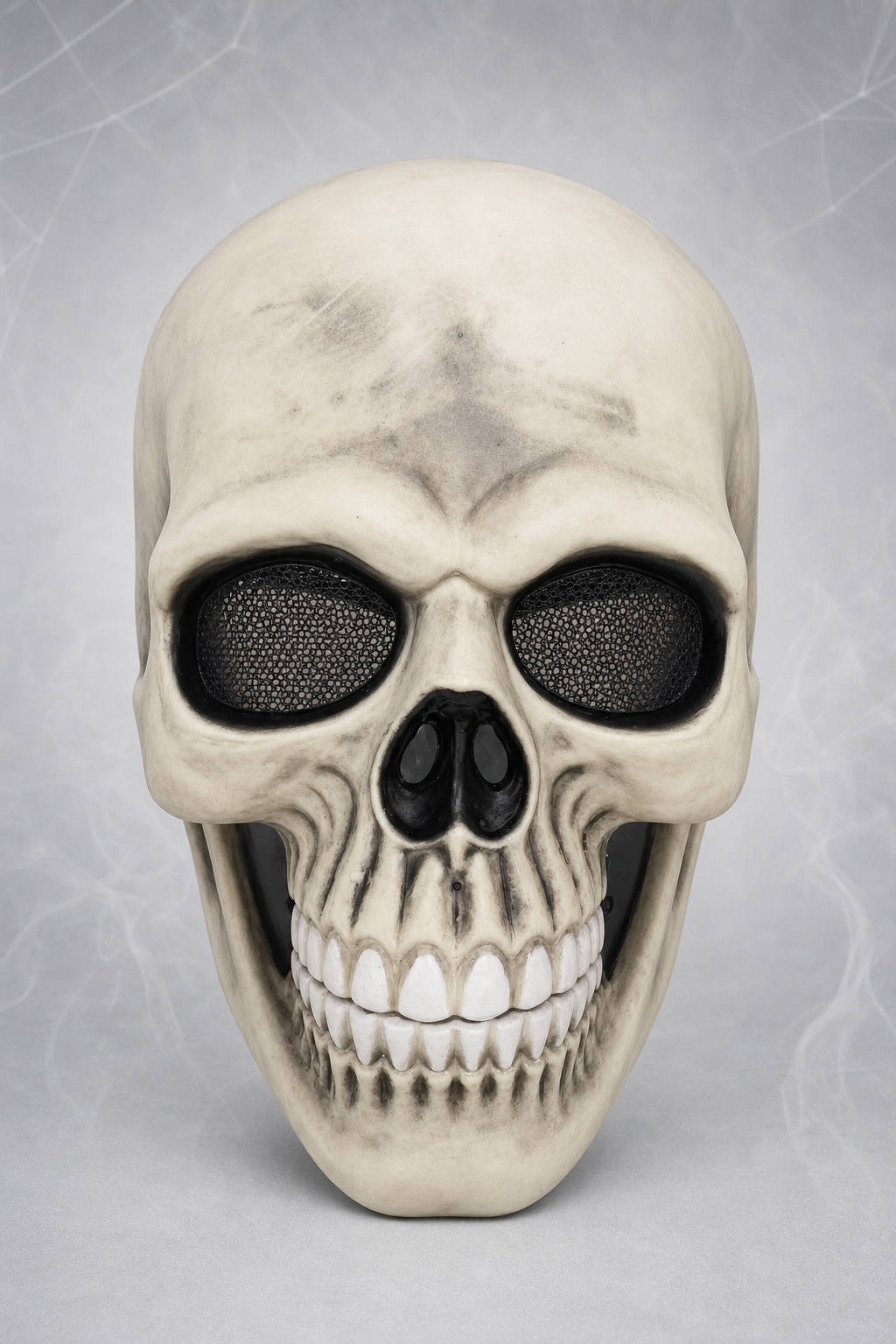 Skull mask with a cream-colored plastic look, black mesh eye openings, hollow nose, and rows of sculpted teeth in a front view