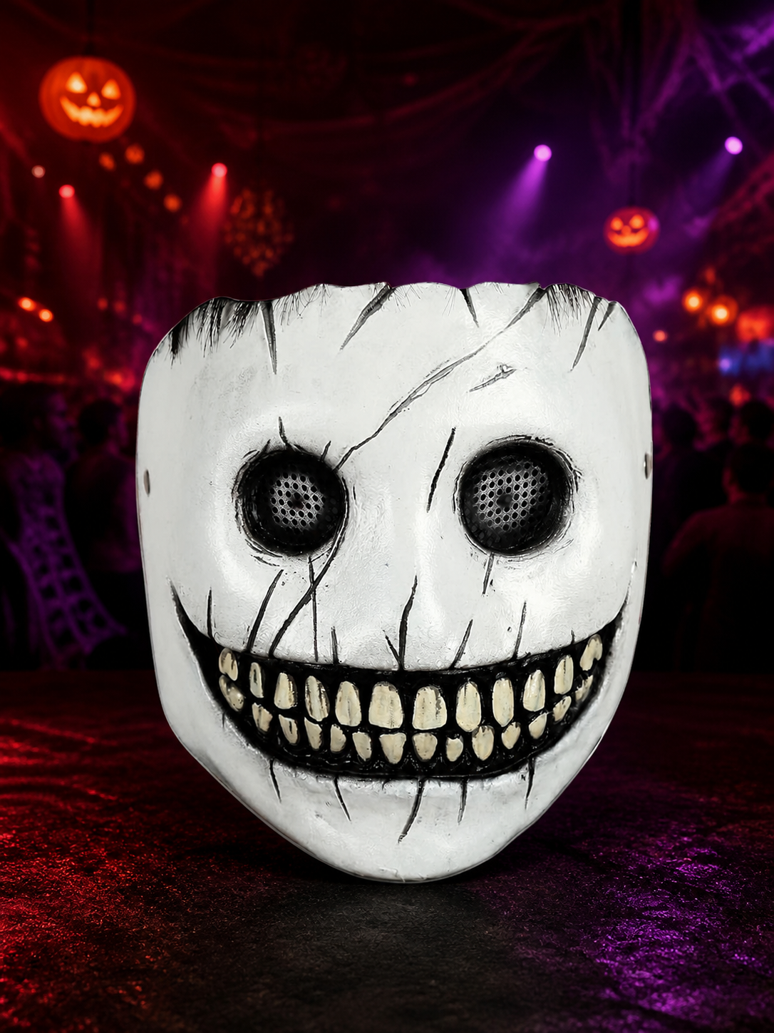 White grinning full-face mask with black eye mesh and painted cracks, displayed in a colorful Halloween party scene