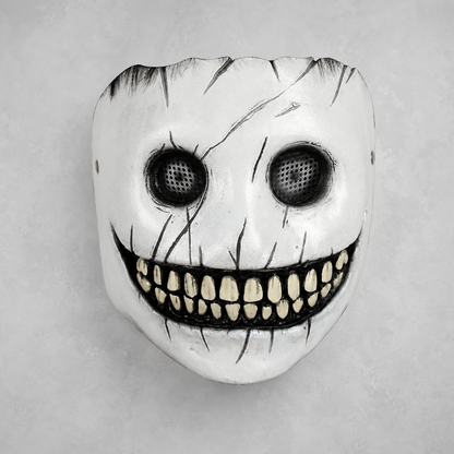 White full-face mask with black eye mesh, painted cracks, and a wide grin showing rows of yellowed teeth, shown against a gray background