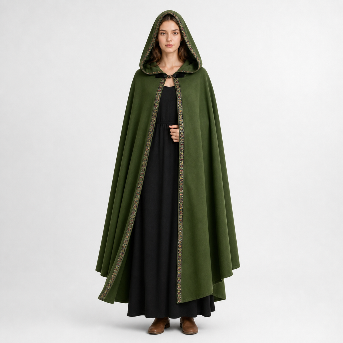 Green hooded cape with patterned trim shown full-length on a model over a black dress with brown ankle boots