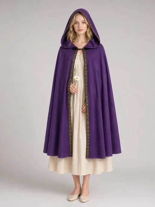 Purple hooded cape with patterned trim, shown full-length on a model over a cream dress