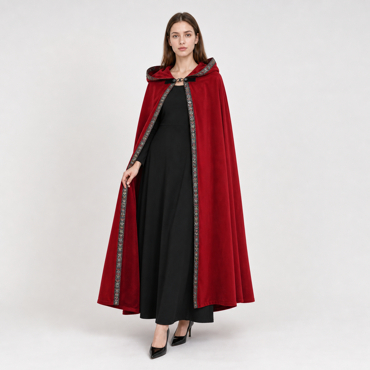 Red velvet-like hooded cloak shown full-body on a model, with patterned trim along the open front and a clasp at the neck