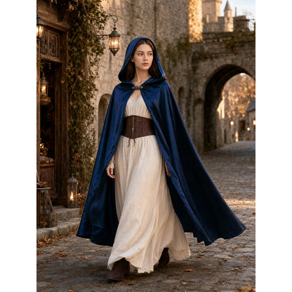 Blue satin-look hooded cape modeled outdoors over a cream dress, showing the front clasp and flowing full-length shape