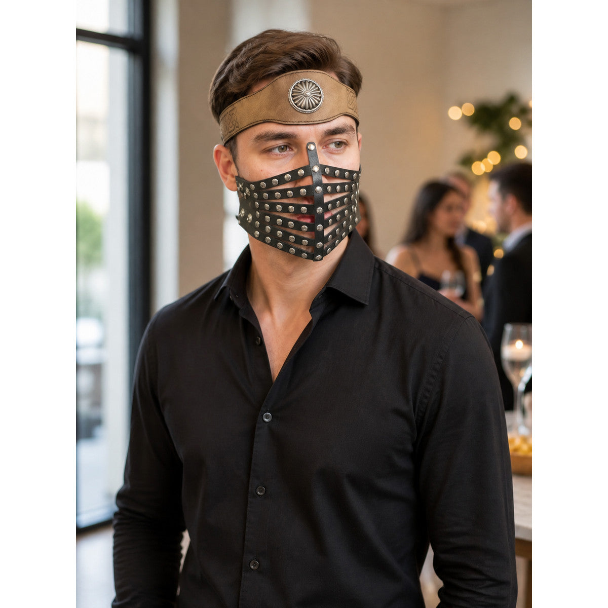 Brown headband and black studded face mask worn by a male model in a black shirt, shown in a styled indoor scene