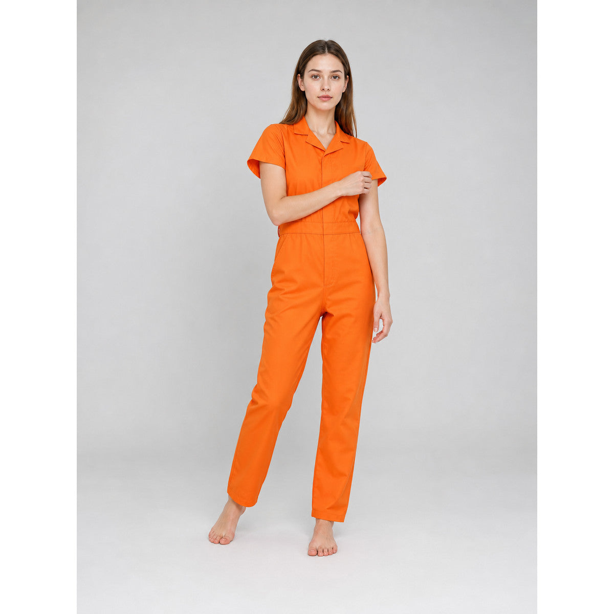 Orange short-sleeve jumpsuit shown on a standing model, featuring a collared neckline, front closure, fitted waist, and straight legs