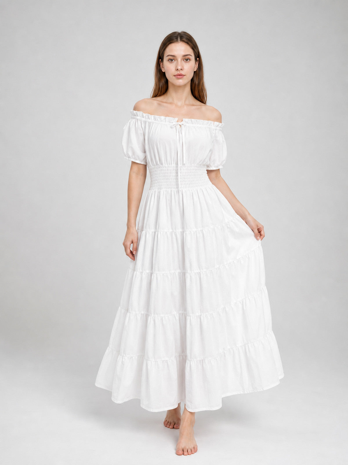 White off-shoulder tiered maxi dress on a standing model, shown from the front with short puff sleeves, a fitted smocked waist, and flowing skirt