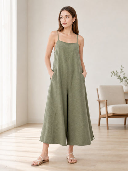 Olive green wide-leg jumpsuit with thin straps and side pockets, shown full-body on a model in a bright room