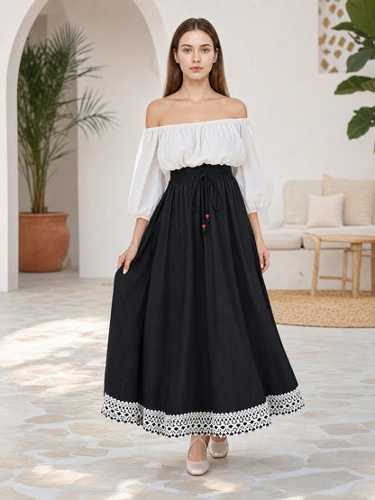 Full-body model wearing a flowing black maxi skirt with a gathered waist, red bead drawstrings, and white lace hem trim in a living room