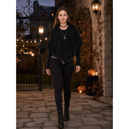 Black hooded knit poncho with long fringe, shown full-body on a model in a lantern-lit outdoor setting
