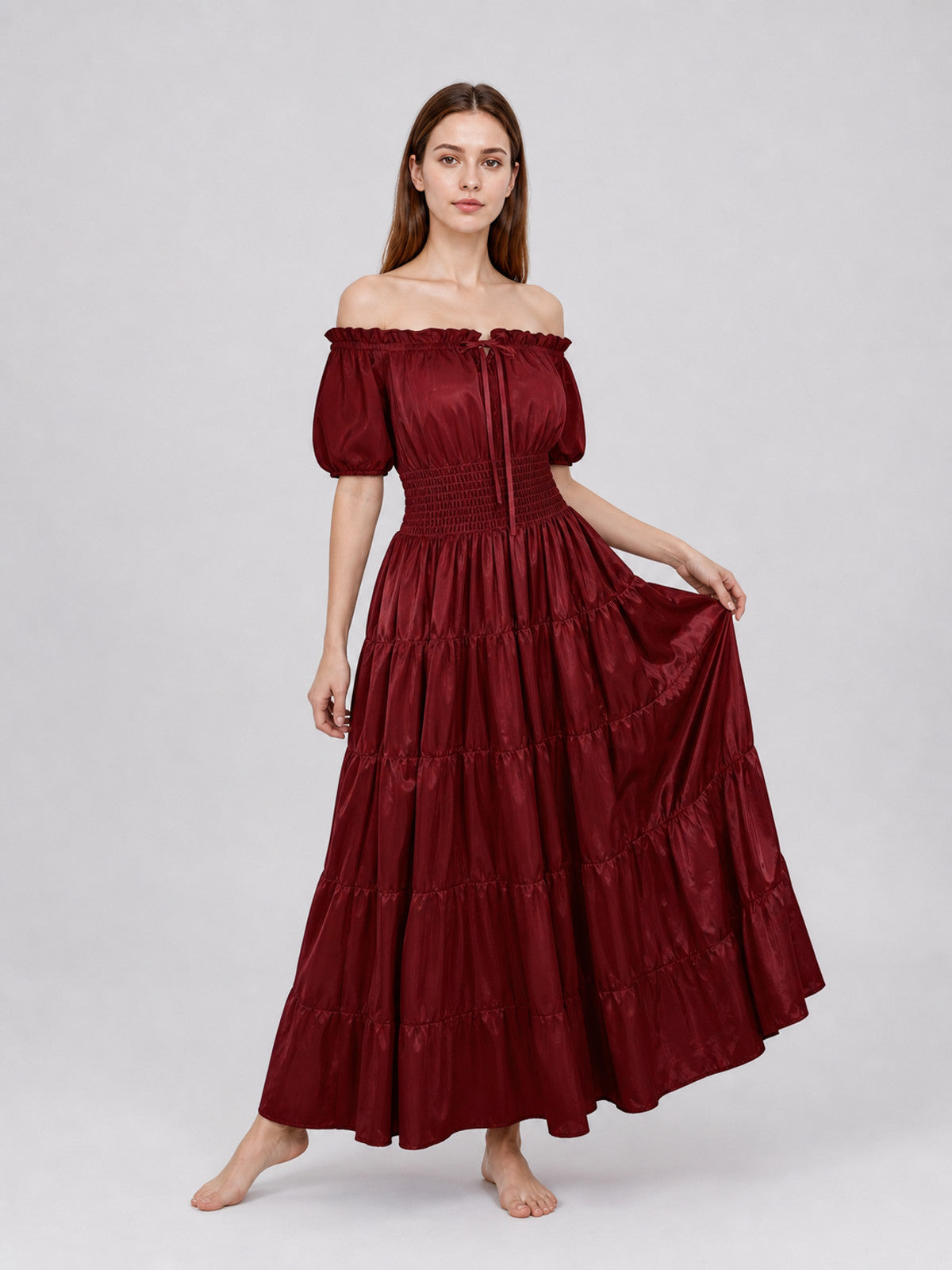 Front three-quarter view of a wine red off-the-shoulder dress with puff sleeves and a tiered skirt held out by the model