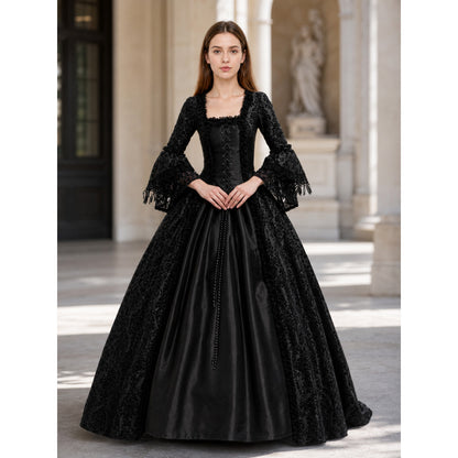 The black dress is designed in the aesthetic of a Victorian-era Gothic costume. The model features a floor-length silhouette, a fitted bodice with a square neckline, and decorative lacing or trim on the front. The long flared sleeves end in