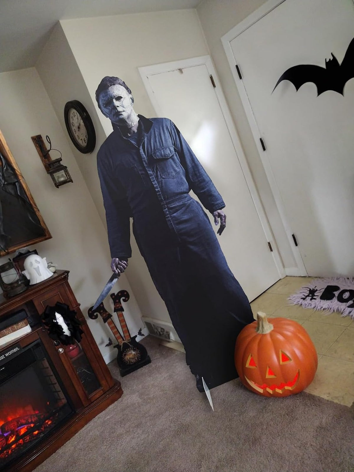 Life-size Michael Myers horror cutout standee displayed indoors next to a fireplace and pumpkin