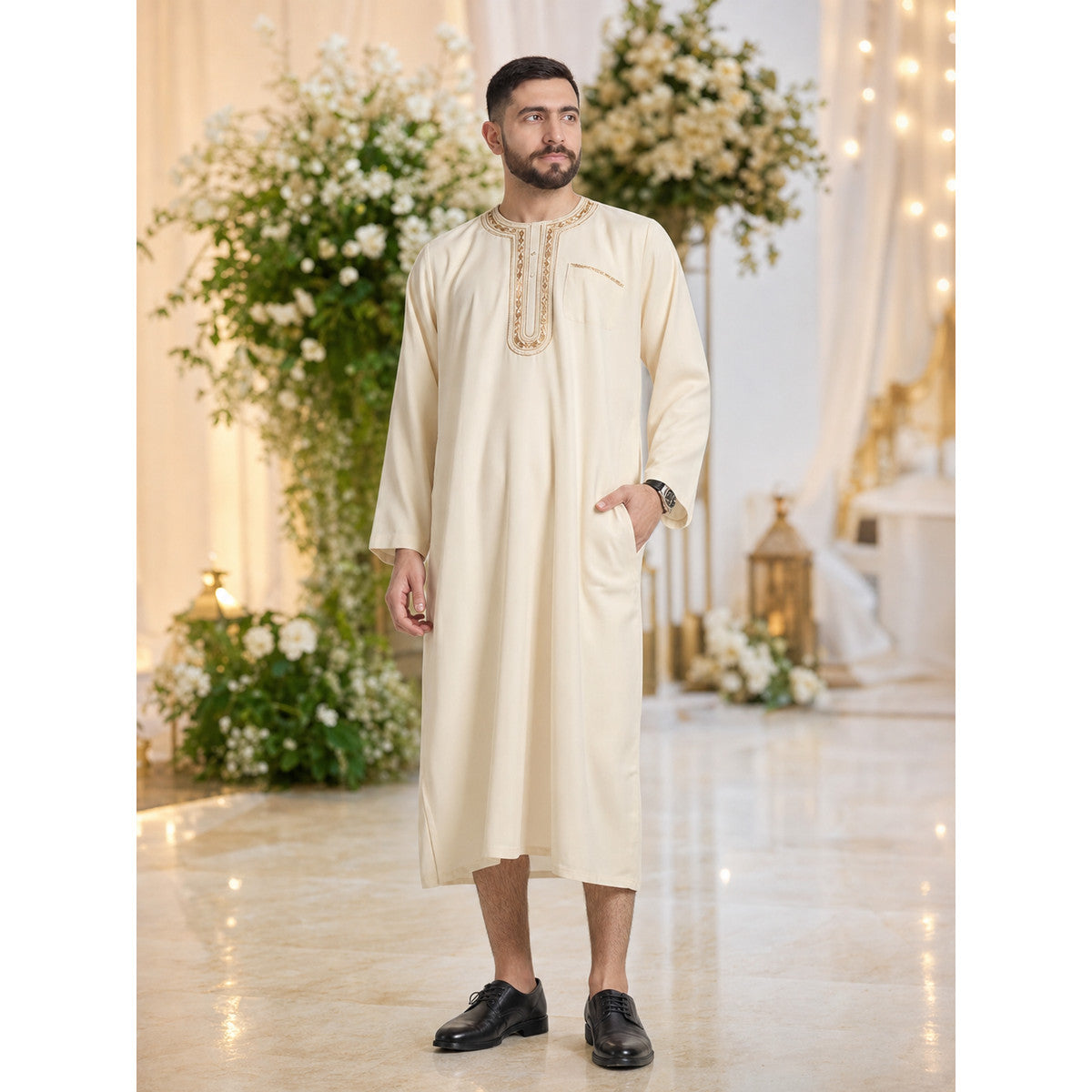Cream embroidered long tunic robe with a chest pocket and side pocket, shown full-body on a model in a decorated indoor setting