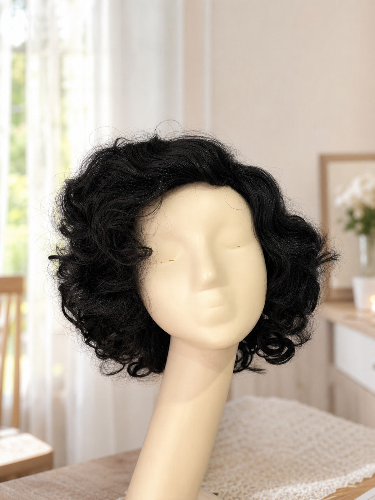 Black curly wig with layered waves displayed on a mannequin head in a bedroom setting