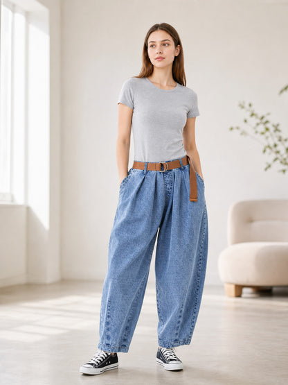 Full-body model wearing blue denim pants with a high waist, wide legs, side pockets, and a brown belt in a bright room
