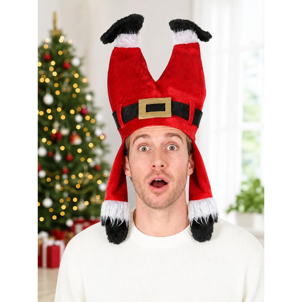 Red plush costume hat modeled from the front with black and white fuzzy trim and a gold buckle, shown in a Christmas-decorated room