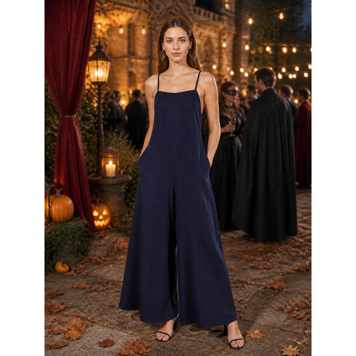 Dark blue wide-leg jumpsuit with thin straps and side pockets, modeled outdoors at a candlelit Halloween-themed gathering