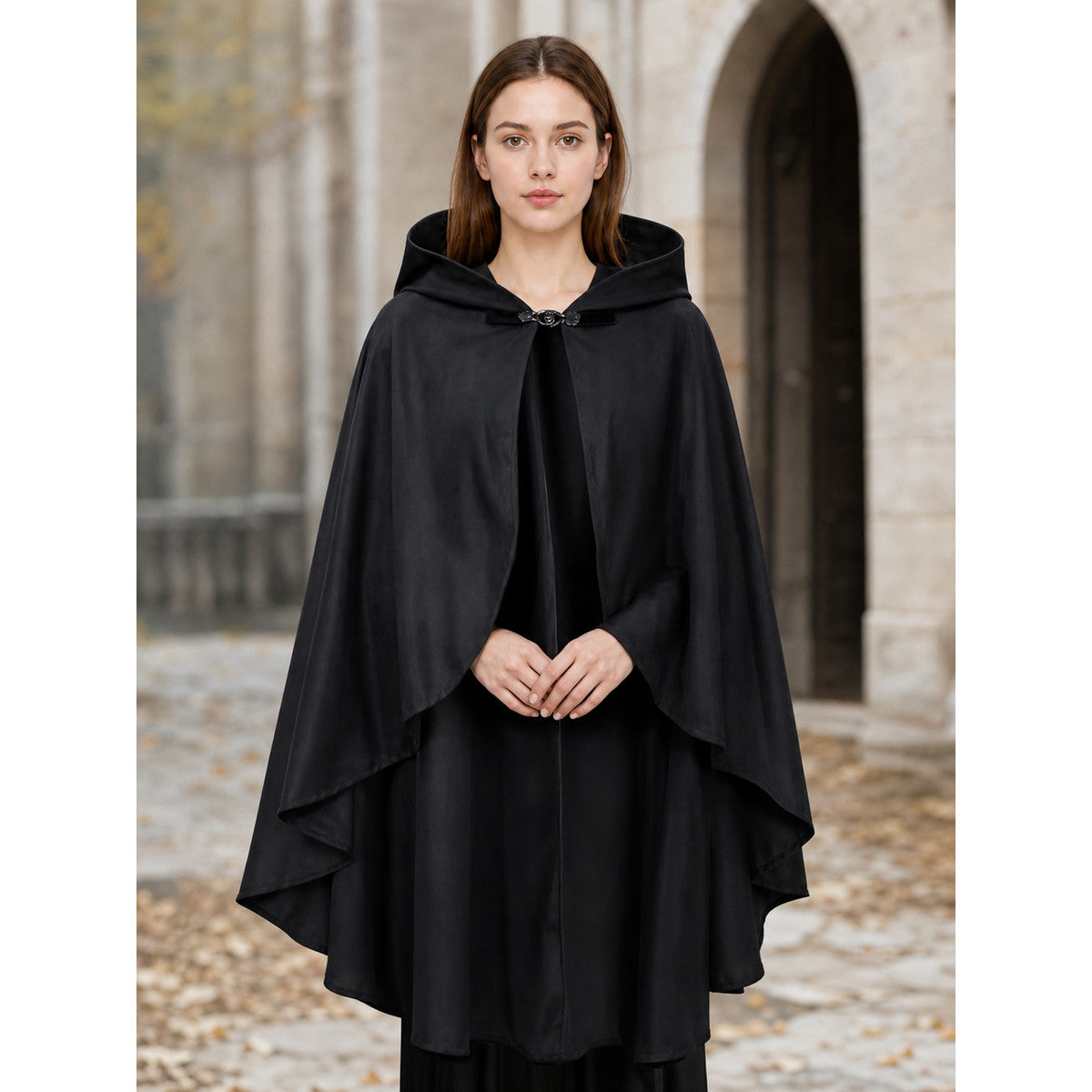 Black hooded cape with a front clasp and layered draped edges, modeled outdoors in front of a stone building