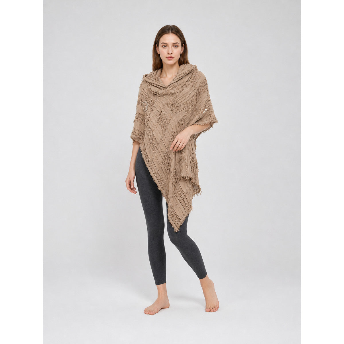 Khaki hooded poncho cape with crinkled woven texture and pointed fringed hem, worn over a black top and leggings