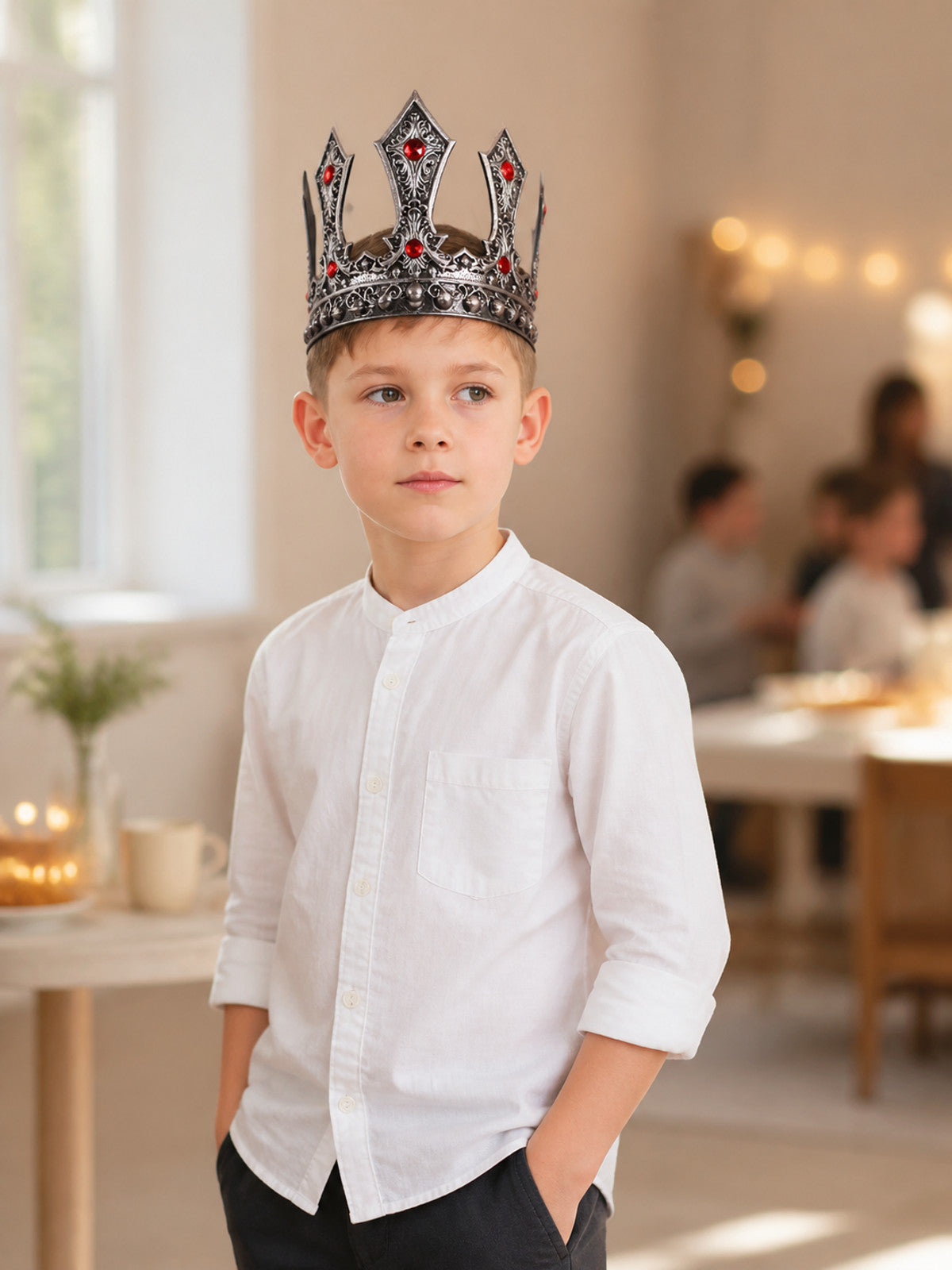 Silver-tone ornate crown with red stones and rounded studs shown on a child in a styled indoor scene