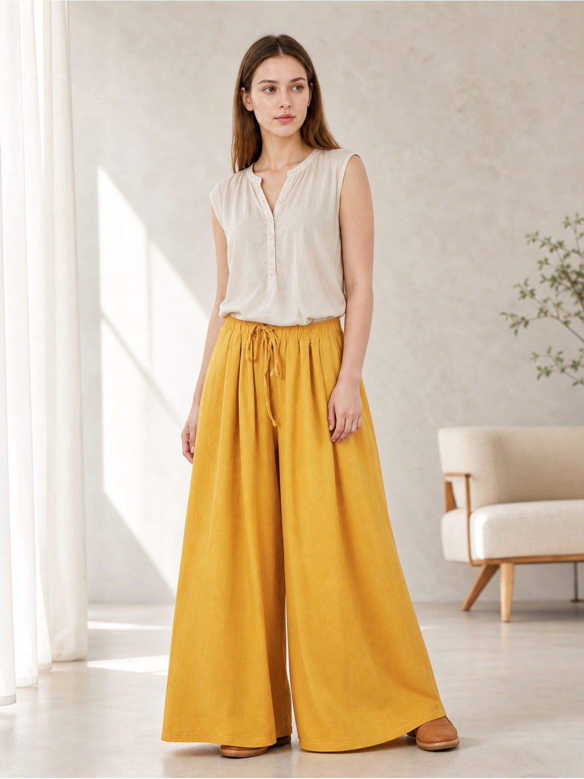 Mustard yellow wide-leg pants styled on a standing model, showing the gathered drawstring waist and floor-length flowing legs