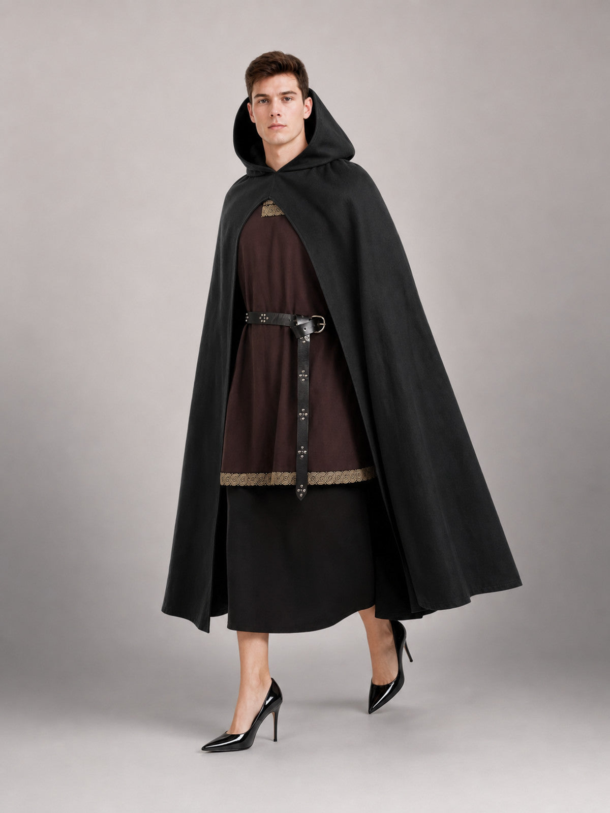 Black hooded cloak shown full-body on a model, with a wide draped silhouette over a brown tunic and black skirt