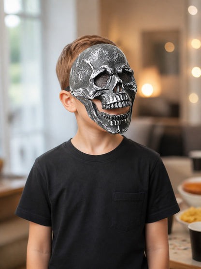 Black skull face mask with raised teeth and textured surface, shown from a side angle on a child in a home setting