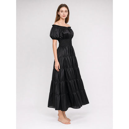 Side view of a black off-shoulder maxi dress on a full-body model, showing short puff sleeves, a fitted waist, and gathered skirt tiers