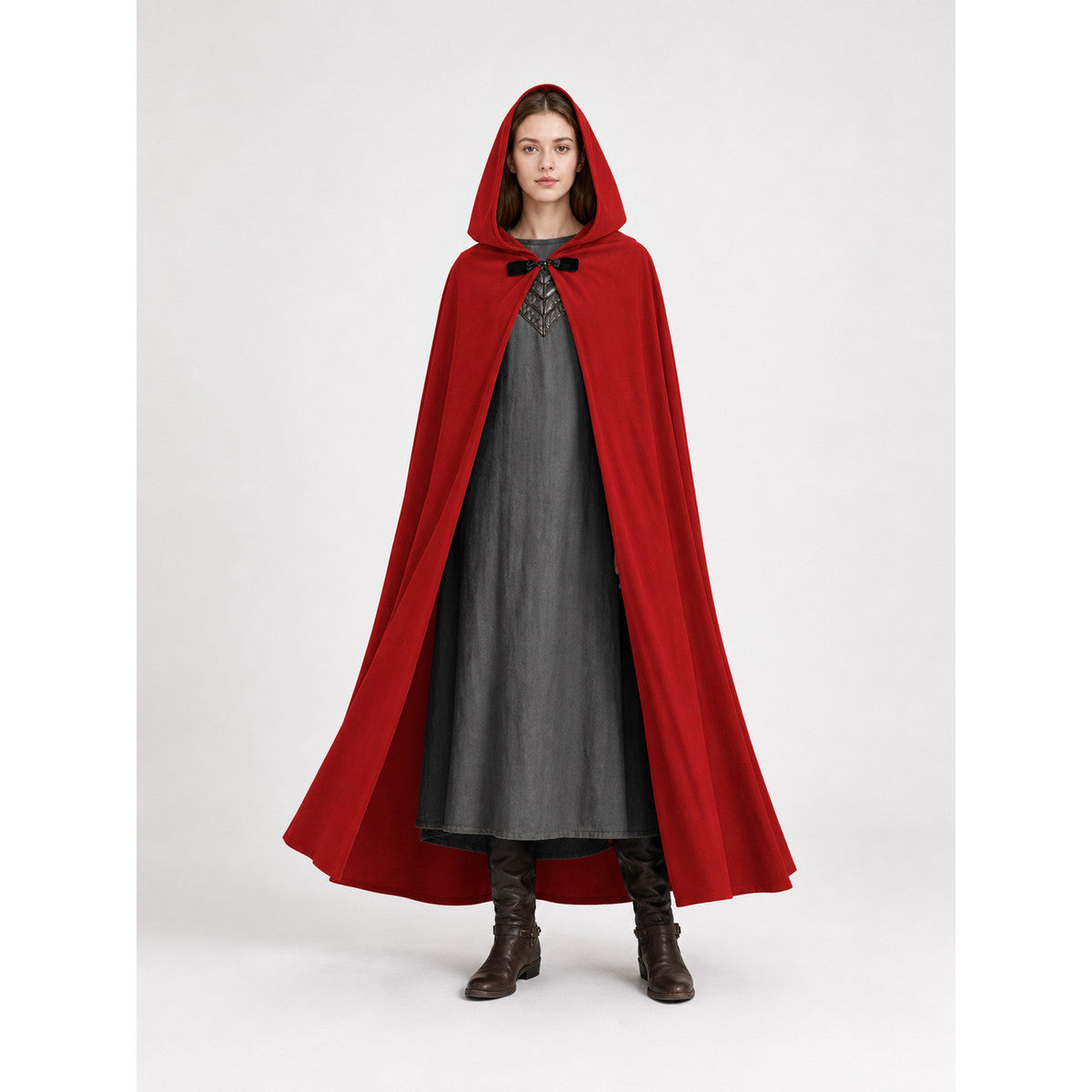 Red hooded cape with a front toggle and long curved hem, shown full-body on a model wearing a gray dress