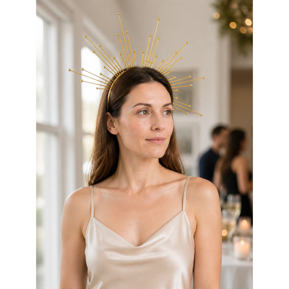 Gold-tone metal halo headpiece with radiating rays and ball tips, shown on a model in a softly lit indoor setting