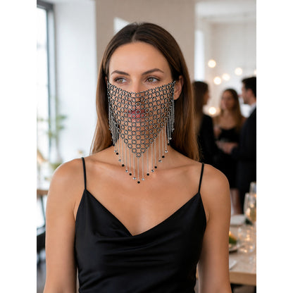 Black and silver chain mesh masquerade mask worn with a black dress in a styled indoor scene, shown from the front