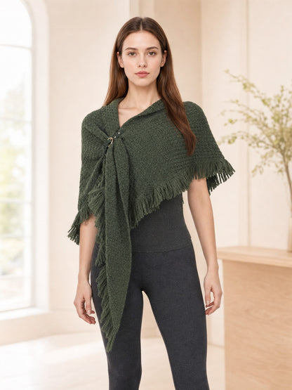 Olive green knitted shawl with long fringe and front fastening, shown on a model in a styled indoor scene