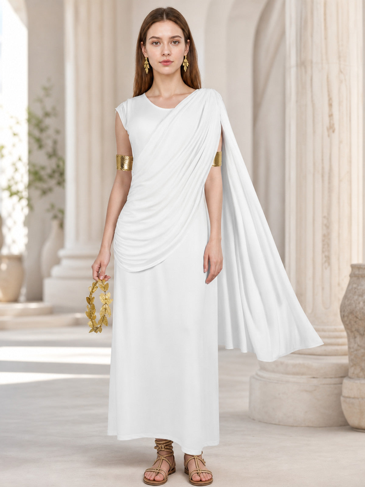 Full-body model wearing a white draped dress with a long train in a columned interior, holding a gold leaf accessory
