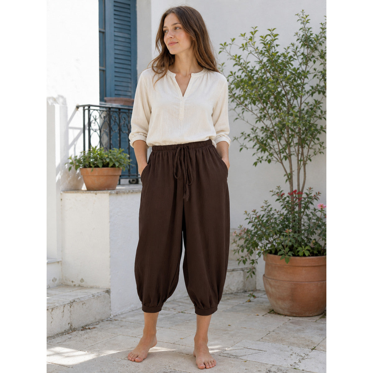 Brown cropped harem pants worn by a model outdoors, with a relaxed fit, elastic drawstring waist, side pockets and gathered cuffs