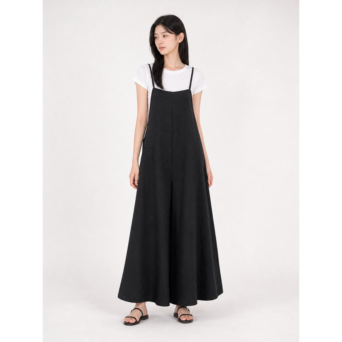 Loose black bib overalls with thin shoulder straps. The design features a simple solid black color and a straight, wide-leg silhouette with long pant legs. The upper portion is styled as a bib, while the thin shoulder straps complement the 