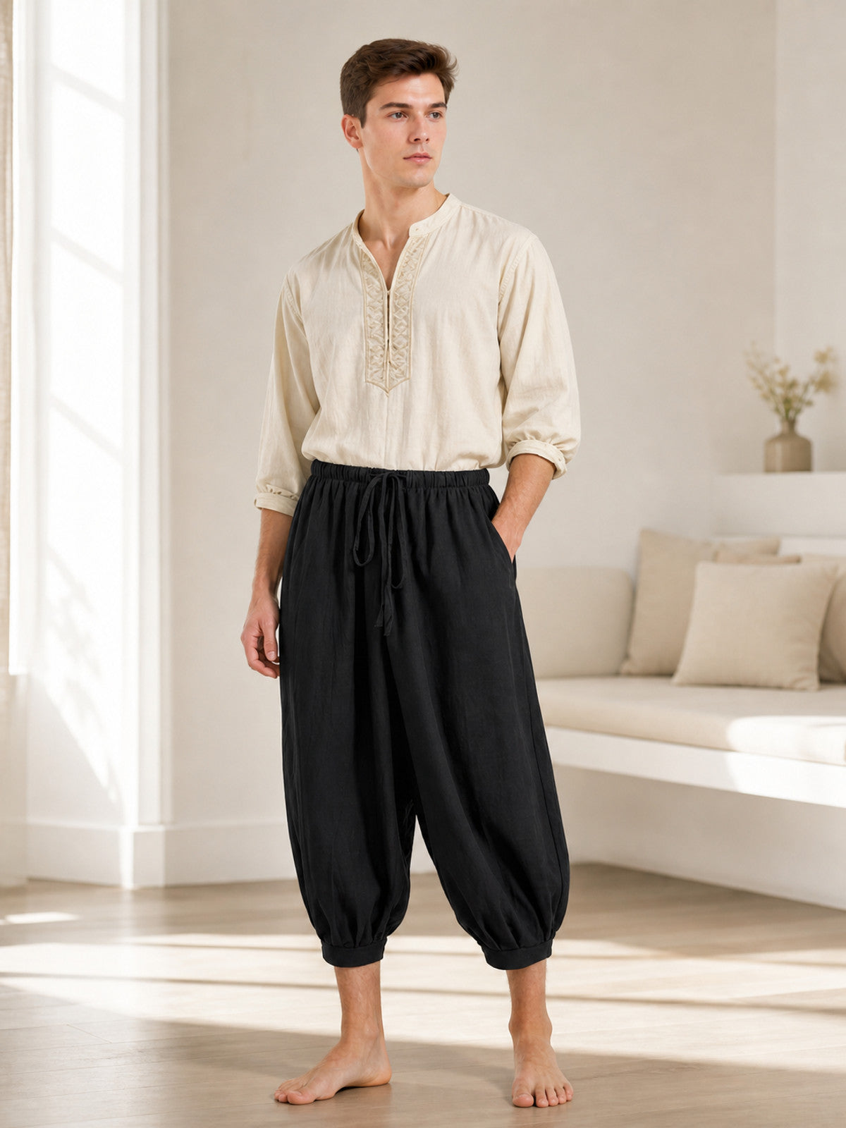 Full-body man wearing black cropped harem pants with a drawstring waist and side pockets in a bright living room