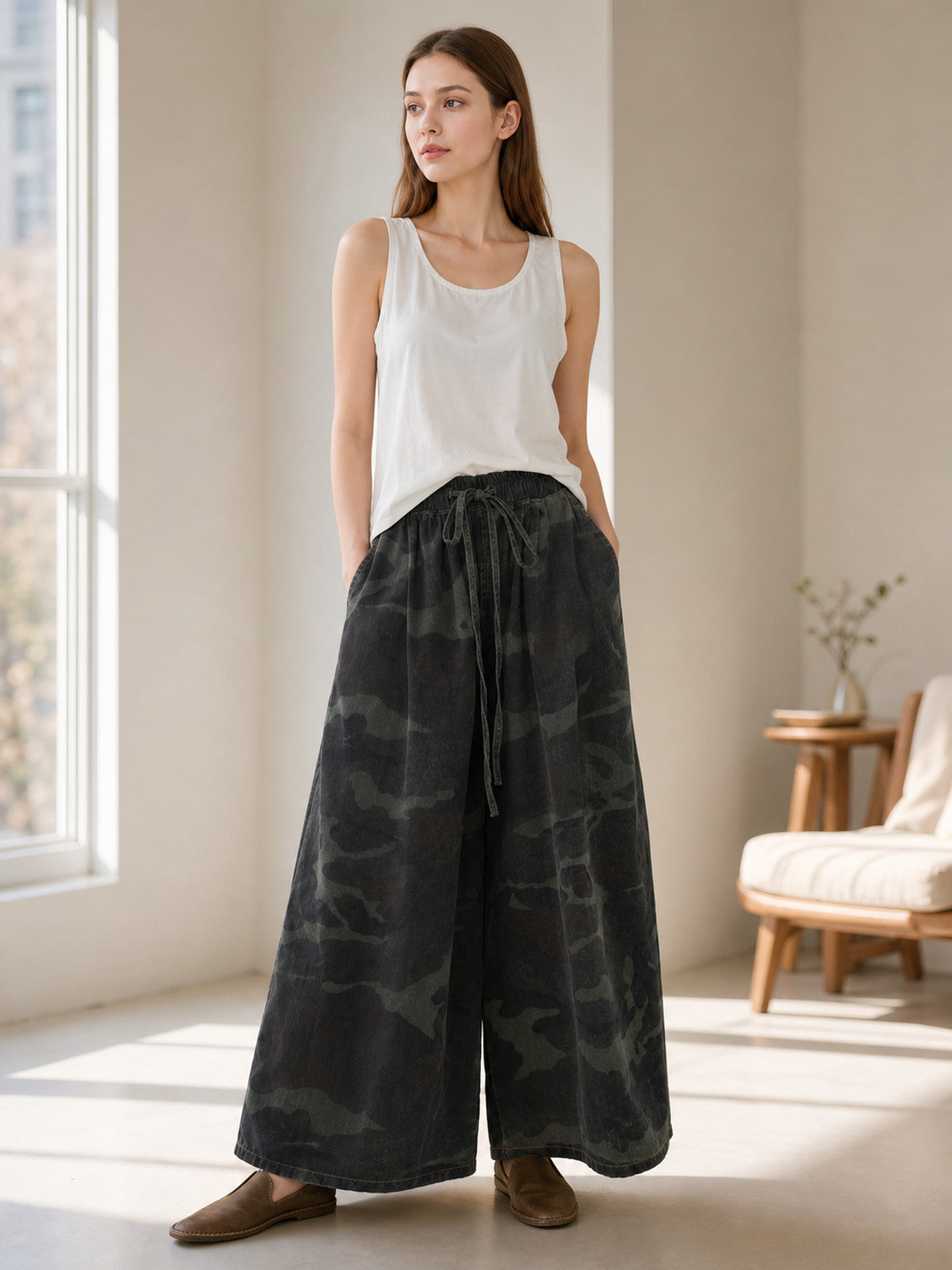 Dark camouflage wide-leg cropped jeans shown on a model indoors, paired with a white tank top and brown flats